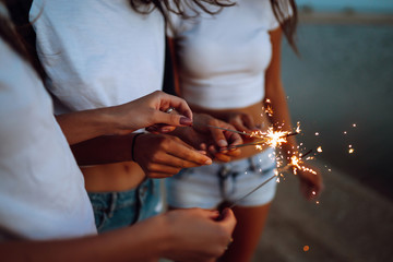 The sparklers in the hands of young girls on the beach. Three girls enjoying party on beach with sparklers. Summer holidays, vacation, relax and lifestyle concept.