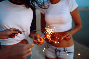 The sparklers in the hands of young girls on the beach. Three girls enjoying party on beach with sparklers. Summer holidays, vacation, relax and lifestyle concept.