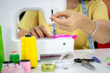 Hand of female fashion designer sewing in studio, seamstress working at working place in fashion workshop with sewing accessory and tailor equipment, sewing machine, bobine de fil, colorful fabrics, h