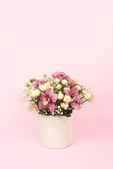 Beautiful bouquet of orchids, roses and gypsophila, Baby's-breath flowers in decorative paper tube packaging on pink background with copy space. Selective focus, celebrating or delivery flower concept