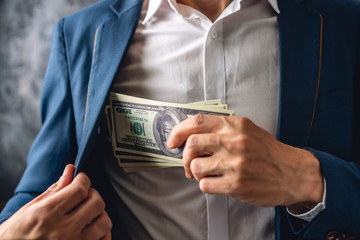 Man in suit putting a wad of hundred-dollar bills in the inside pocket of his jacket. Concept of corruption and bribery