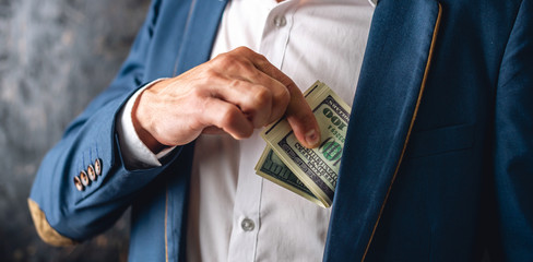 Man in suit putting a wad of hundred-dollar bills in the inside pocket of his jacket. Concept of...