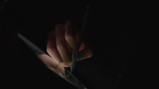 Close up hand of artist drawing on a digital tablet with pencil in dark room without light.
