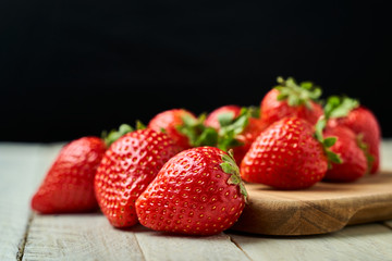 Red strawberries on a wooden board with a dark background.