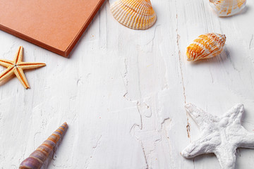 Brown open notepad surrounded by sea shells on white wooden table closeup