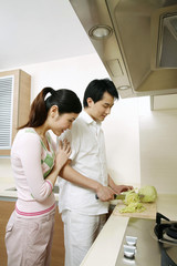 Man cutting vegetables in the kitchen, woman standing by the side