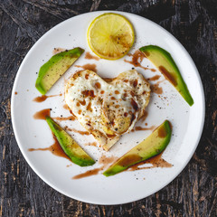Healthy romantic Breakfast of fried eggs in the shape of a heart with slices of avocado on a white plate. Top view