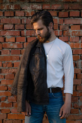 Bearded man posing against a brick wall.
