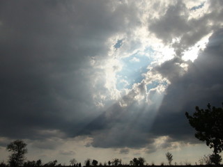 Unique natural picture of direct sunlight surrounded by dark rain clouds in the changing spring sky.