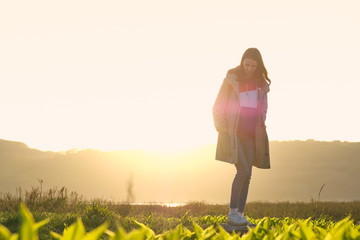 Fototapeta premium Close up young girl balancing on a wooden log in the middle of a green field in the sunset rays. Journey and outdoor concept.