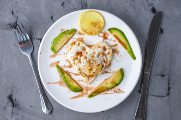 Healthy romantic Breakfast of fried eggs in the shape of a heart with slices of avocado on a white plate. Top view