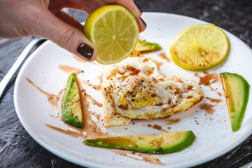 Healthy romantic Breakfast of fried eggs in the shape of a heart with slices of avocado on a white plate.