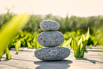 Balance pebbles on a wooden deck with green foliage background at sunset rays. Spa and meditation concept.