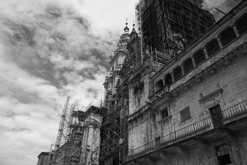 Front facade of the cathedral in Santiago de Compostela during restoration with scaffolding under a cloudy sky in black and white