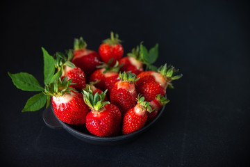 Fresh juicy strawberries in a black plate on a black matte background