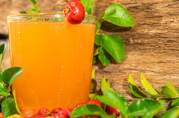 Fresh fruits and acerola juice (Malpighia emarginata) between leaves on wooden background