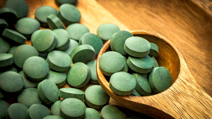 Green algae in tablets - chlorella, spirulina in wooden spoon on wooden background - closeup