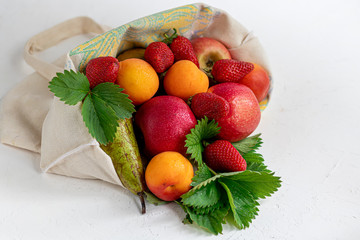 Fresh fruits in an eco cotton bag on a table in the kitchen. with apples and pears, apricots and strawberries, zero waste trading concept. Ban plastic.