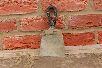The putty knife with traces of concrete mortar is  on the background of a red brick wall. Renovation and repair process.
