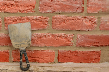 The putty knife with traces of concrete mortar is  on the background of a red brick wall. Renovation and repair process.