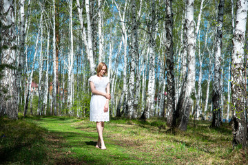 
Young girl in the woods in a white dress. A girl walks in the forest. Girl on a sunny day in the forest.