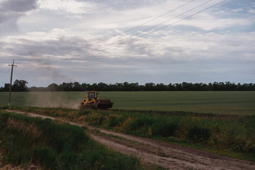 Fototapeta premium Yellow tractor rides on a green field.