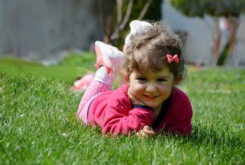 Little Girl Laying on a Green Grass Outdoor. Happy Kid Playing Outdoor 