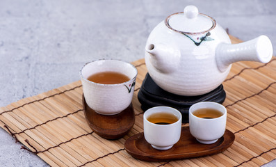 Hot tea in white teapot and cups on a sieve over bright gray cement background, closeup, copy space design concept.