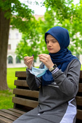 Muslim woman taking off surgical mask while sitting alone in the park