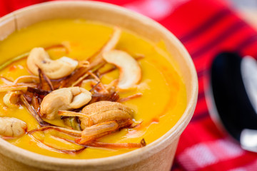 Thai Pumpkin Coconut Curry with cashew Soup in a takeaway container with a red napkin and spoon in the background