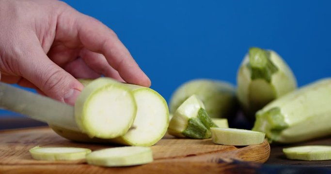 Male hand with knife cut pieces of zucchini on a cutting Board.
