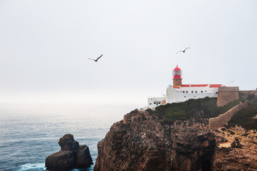 Lighthouse on Cape St. Vincent at misty evening in Algarve, Portugal. Seagulls soaring in the sky....
