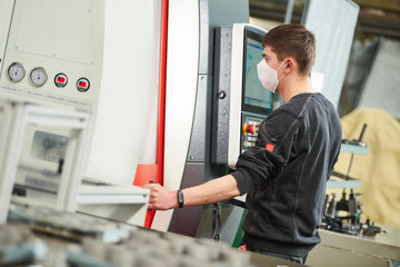 Obraz premium Industrial worker operating cnc machine in protective mask at metal machining industry