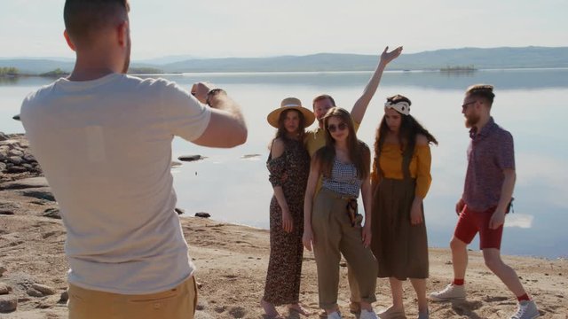 Young Caucasian man talking to group of friends when taking picture of them on sunny day at the beach