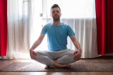 Young man meditating on his living room floor sitting. Stay home and be active.