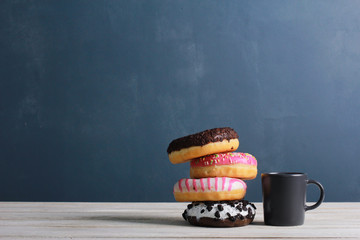 Coffee cup with stack of donuts on white wooden table against dark wall background. Side view, copy space, closeup. Bakery, coffee shop menu, breakfast, break concept