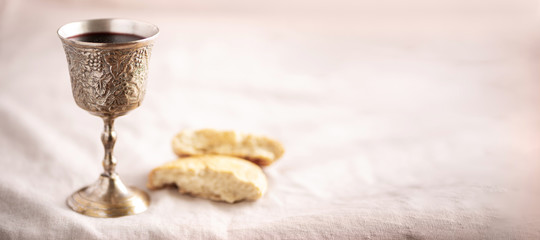 Unleavened bread, chalice of wine, silver kiddush wine cup on canva background. Communion still life. Christian communion concept for reminder of Jesus sacrifice. Easter passover