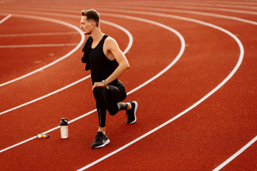 Obraz premium Young handsome man doing stretching before running in the stadium