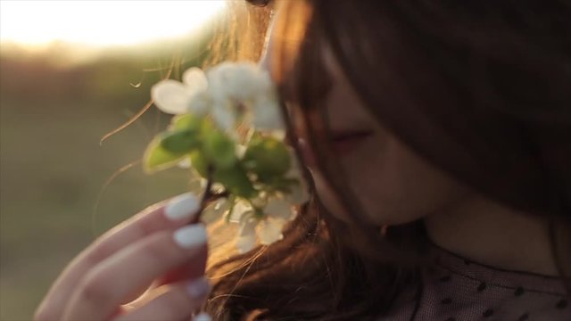 A young girl in a beautiful dress holds in her hand a twig with flowers and inhales the aroma with her eyes closed. Close-up. Slow motion. The camera changes focus