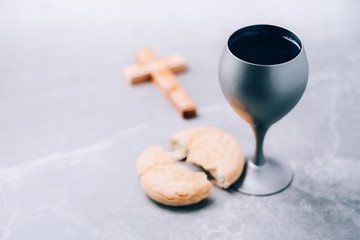 Unleavened bread, chalice of wine, wooden cross on grey background. Christian communion for reminder of Jesus sacrifice. Easter passover. Eucharist concept. Christianity symbol and faith
