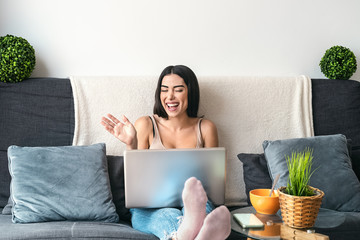 Young woman making video call sitting on sofa - Happy girl having fun doing video conference with...