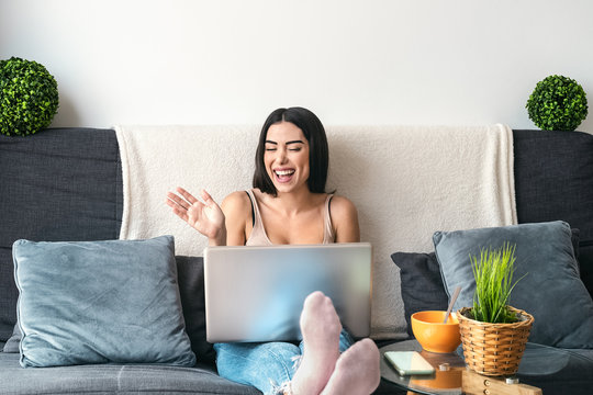 Young woman making video call sitting on sofa - Happy girl having fun doing video conference with family and friends - Youth millennial people lifestyle and technology concept