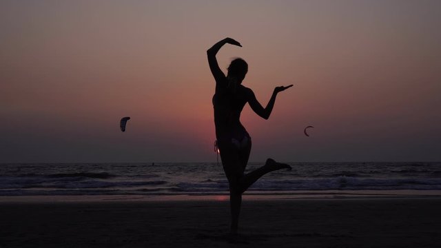 A woman practices yoga at sunset. Silhouette of a girl who does yoga assans