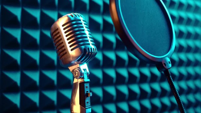 Zoom-out video of retro microphone standing on a stand with pop-up filter, with acoustic foam panel at background, blue light