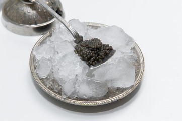 black caviar on a silver tea spoon which lies on  ice cubes