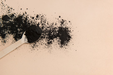 Activated charcoal and wooden spoon on camel color background. Zero waste concept.