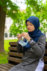 Muslim woman taking off surgical mask while sitting alone in the park