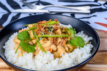 A bowl of Satay Chicken with plain white rice on a wooden board