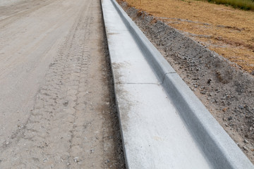 New roadway under construction, extruded concrete curb beside graded dirt road, straw and erosion...