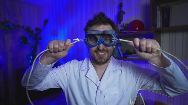 Crazy doctor connects two electrical wires. Hairy Computer nerd with big glasses and a white coat. Funny scientist conducts tests in the laboratory. Electric shock. Medicine concept.